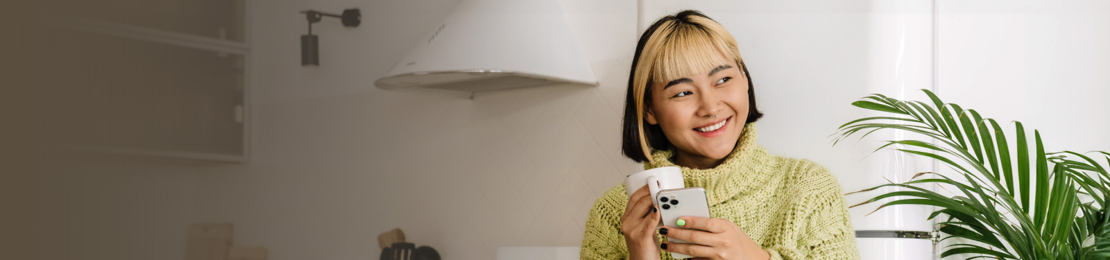 Asian woman drinking holding a coffee mug and mobile phone and smiling.